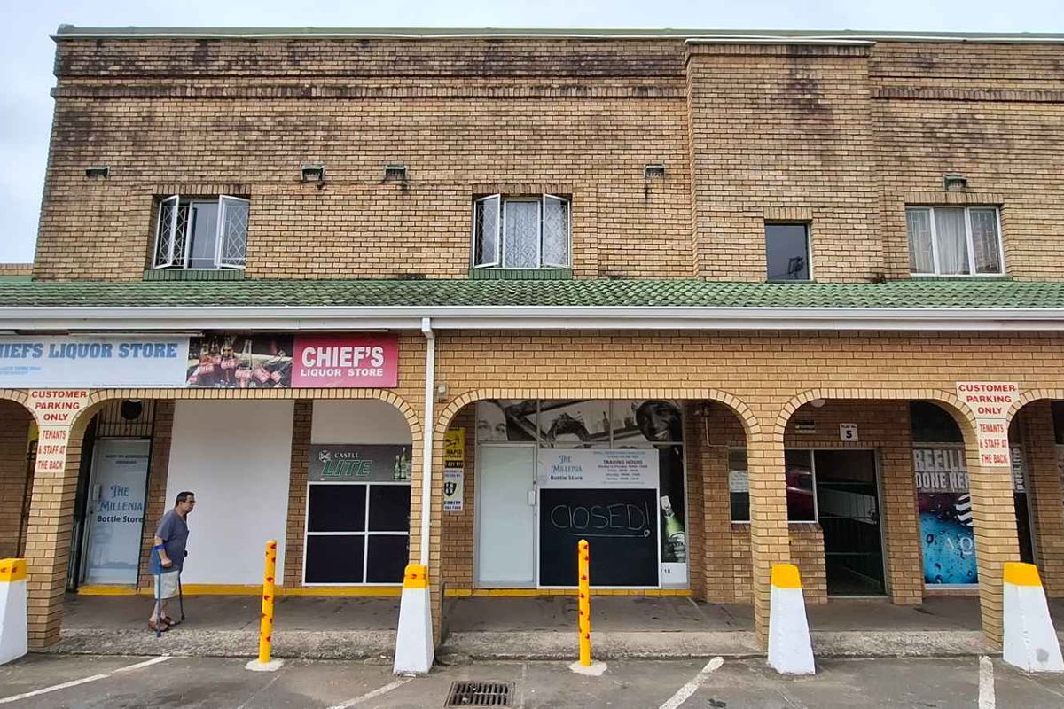Front elevation of a commercial building featuring multiple storefronts, brick facade, and a covered walkway with parking access.