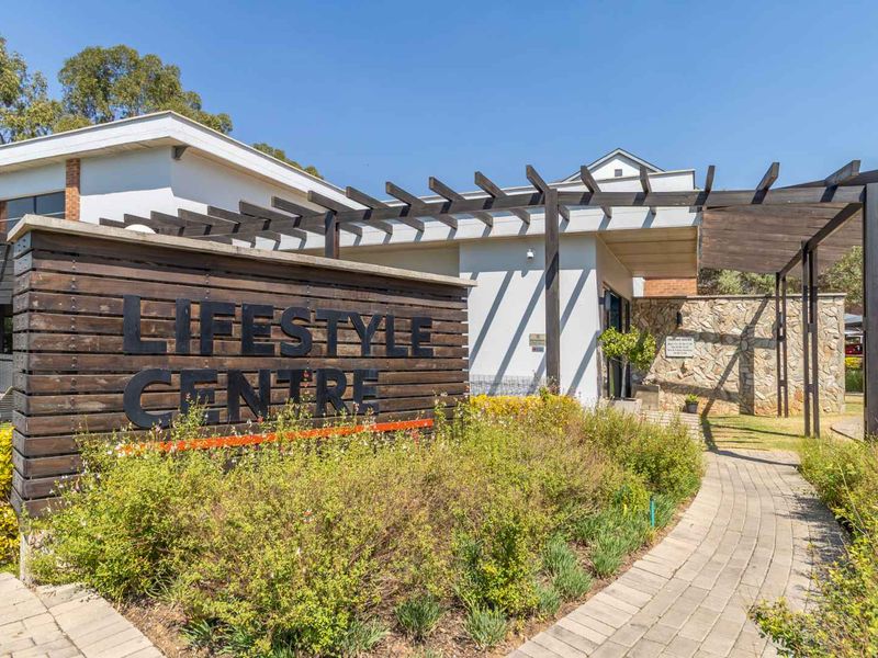 Exterior view of the apartment complex lifestyle centre featuring a timber pergola, stone feature wall, and paved entrance walkway.