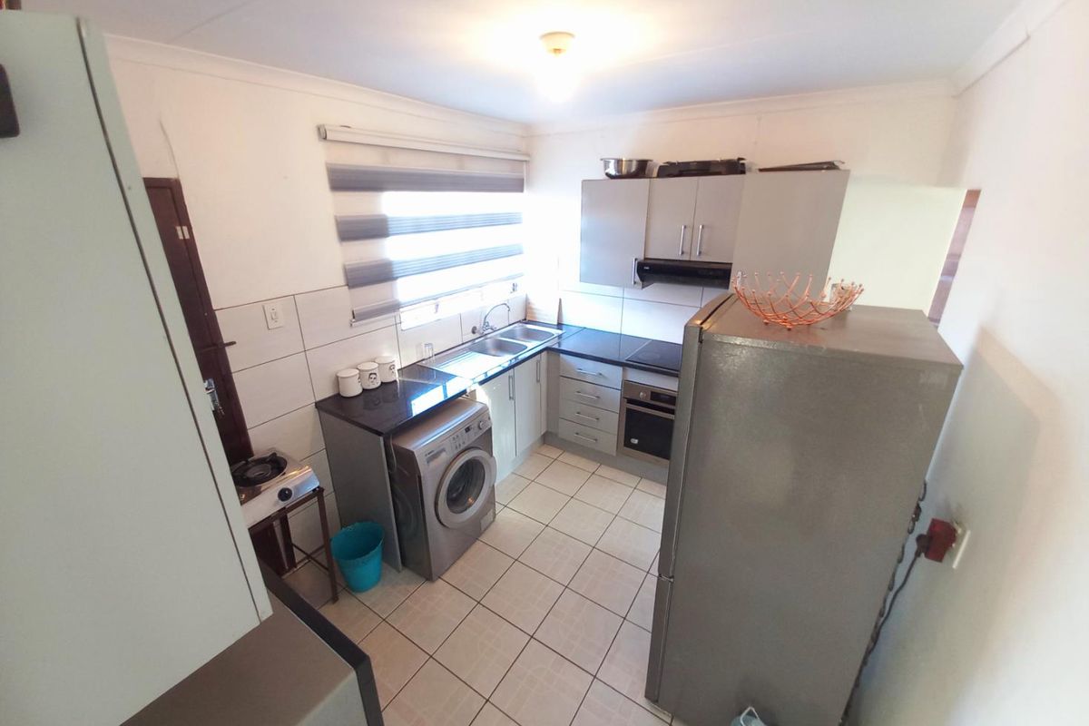 Compact kitchen featuring built-in cabinetry, integrated oven and hob, stainless steel sink, and tiled flooring with space for laundry appliances.