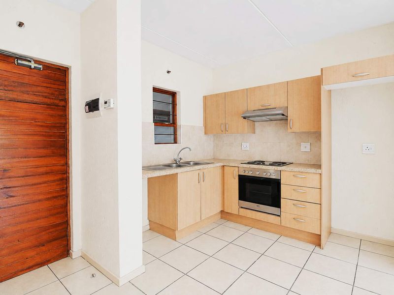 A functional kitchen featuring light wood cabinetry, built-in oven and hob, tiled flooring, and a tiled backsplash, presented in a clean, empty state.