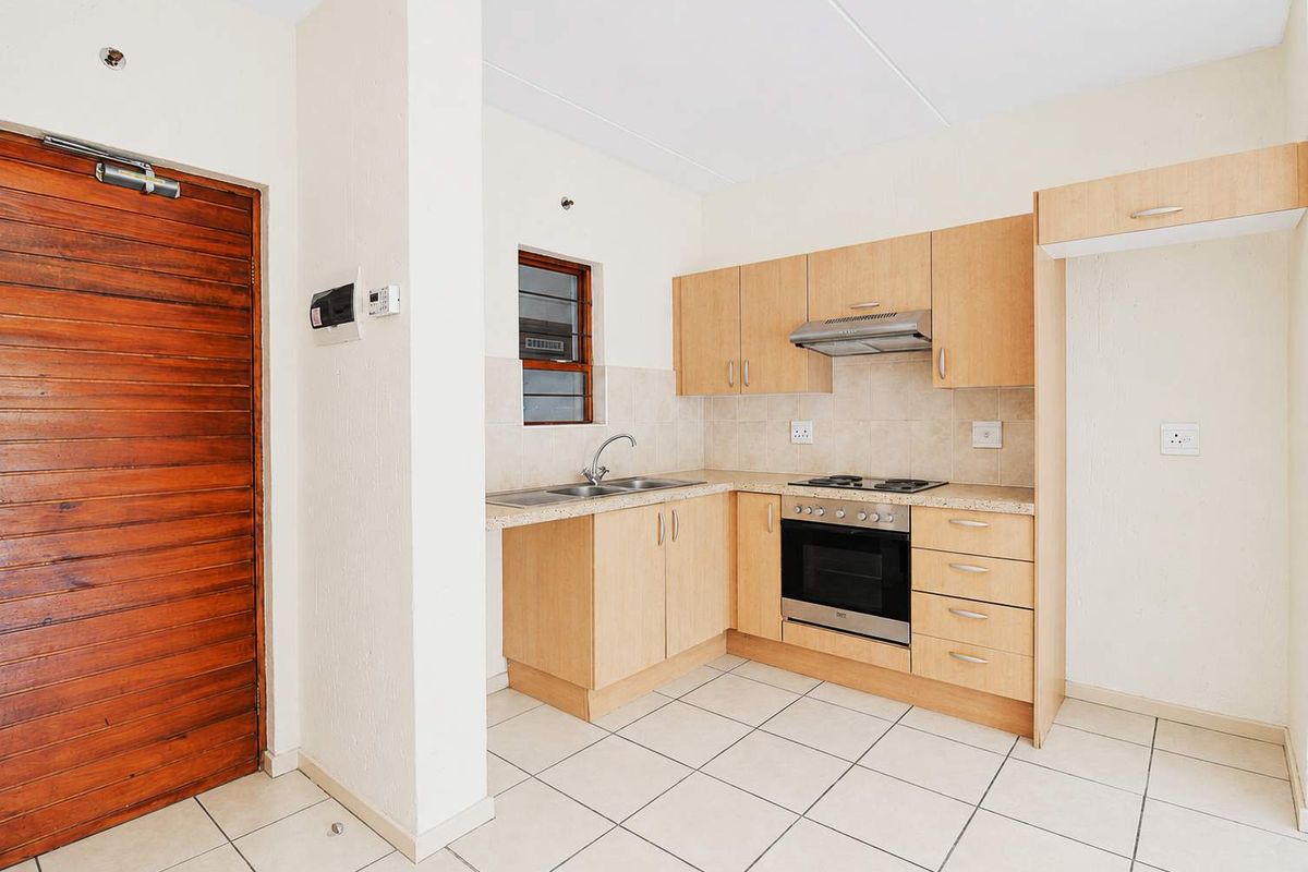 A functional kitchen featuring light wood cabinetry, built-in oven and hob, tiled flooring, and a tiled backsplash, presented in a clean, empty state.