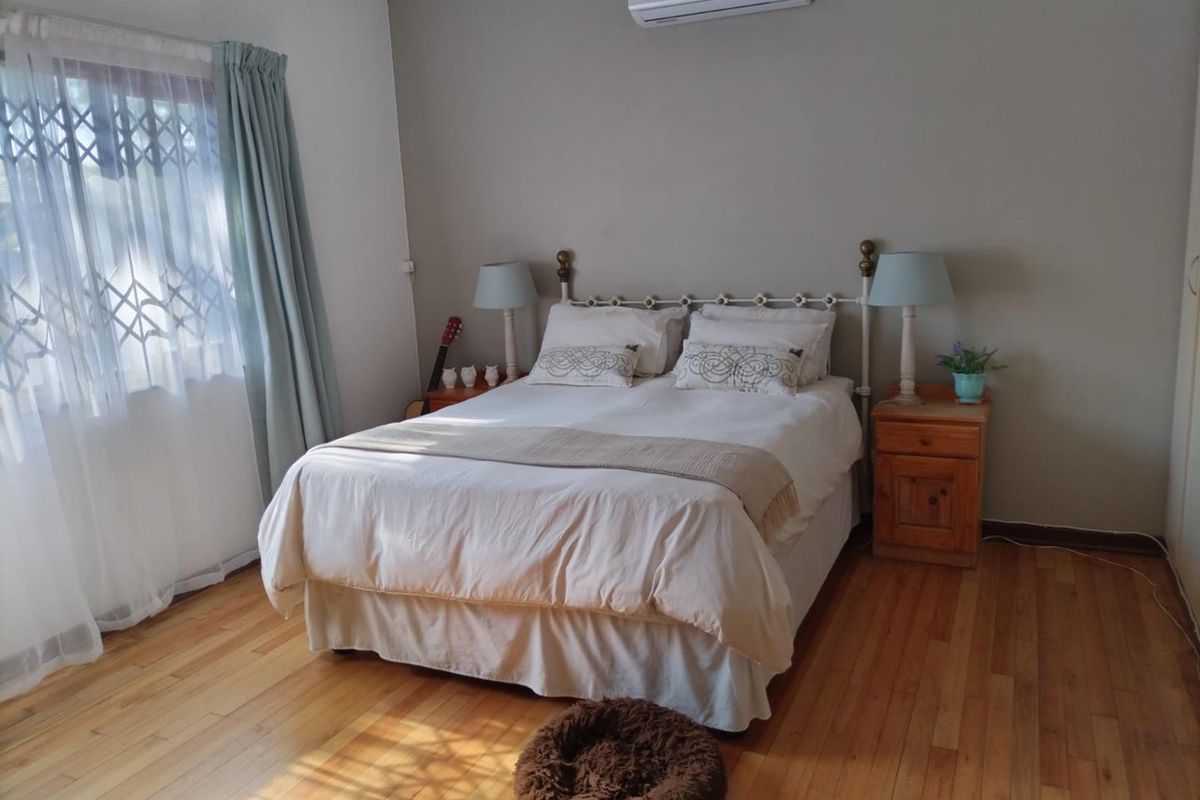A well-maintained bedroom featuring polished hardwood flooring, a wall-mounted split-system air conditioner, and a window fitted with a security gate.