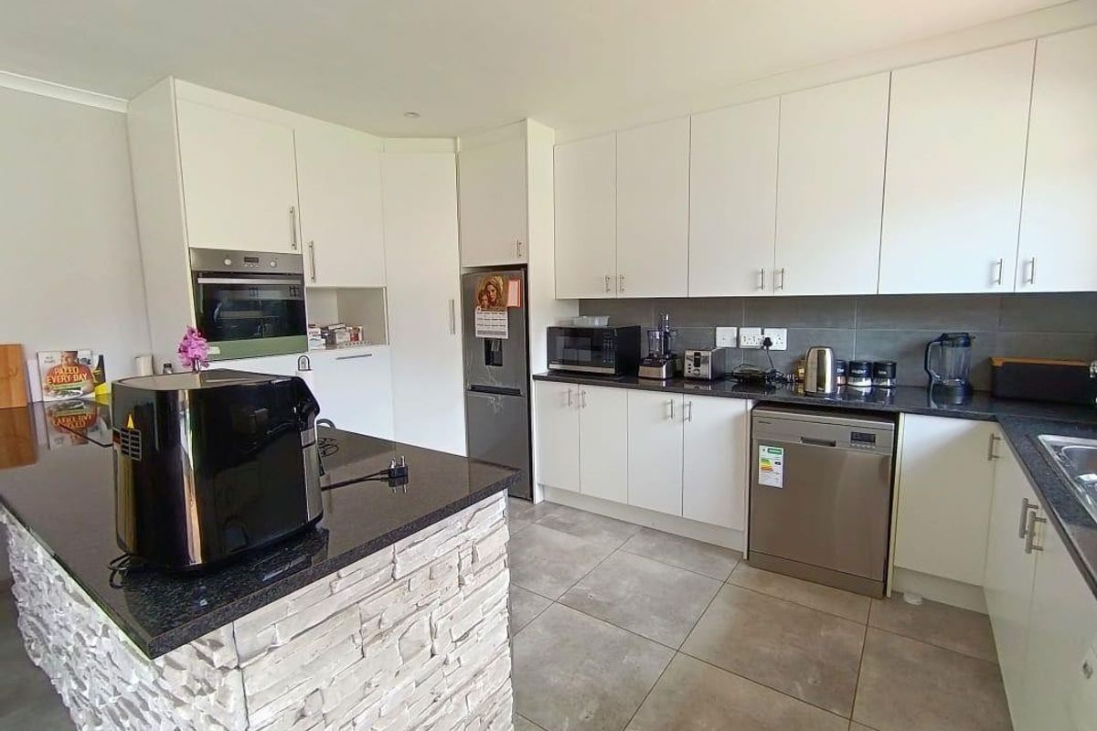 Modern kitchen featuring white cabinetry, dark granite countertops, a stone-clad island, and integrated stainless steel appliances.