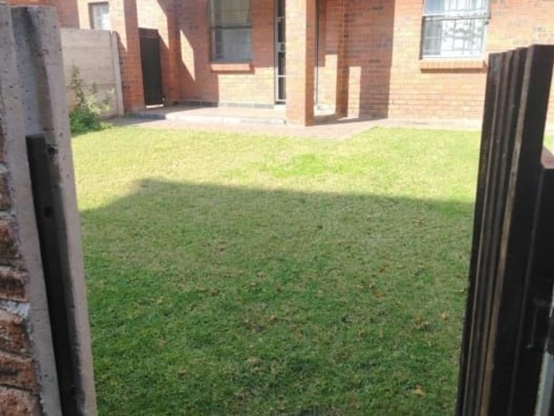 A view of the rear garden area featuring a lawn, paved patio, and brick exterior wall of the apartment.