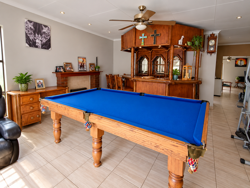 Spacious living area featuring a built-in wooden bar, brick fireplace, ceiling fan, and neutral tiled flooring, offering a versatile entertainment space.