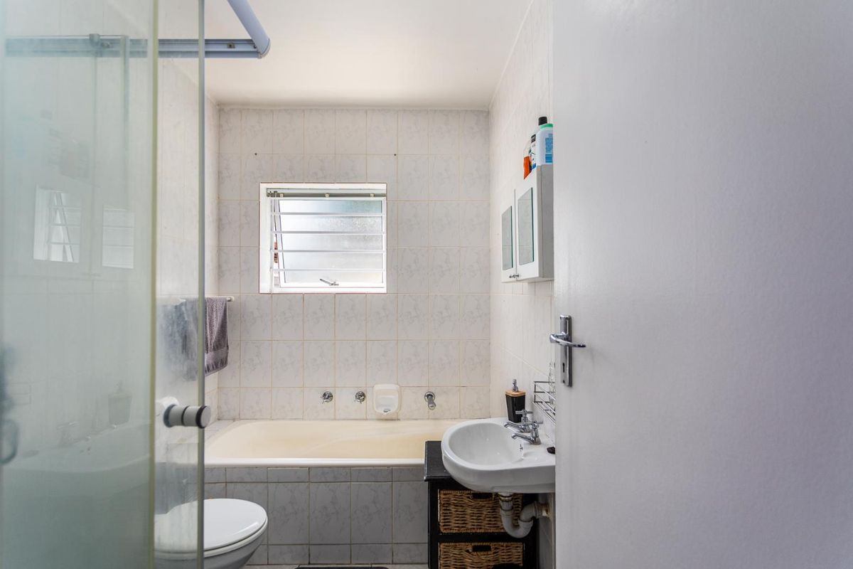 A functional bathroom featuring a built-in bathtub, wall-mounted basin, and tiled finishes, offering a practical layout for an apartment setting.