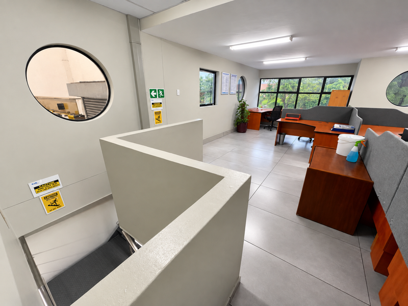 Open-plan office space featuring tiled flooring, porthole windows, and integrated workstation partitions, with an internal staircase providing access to the lower level.