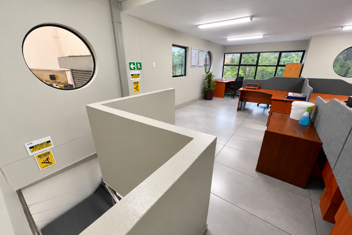 Open-plan office space featuring tiled flooring, porthole windows, and integrated workstation partitions, with an internal staircase providing access to the lower level.