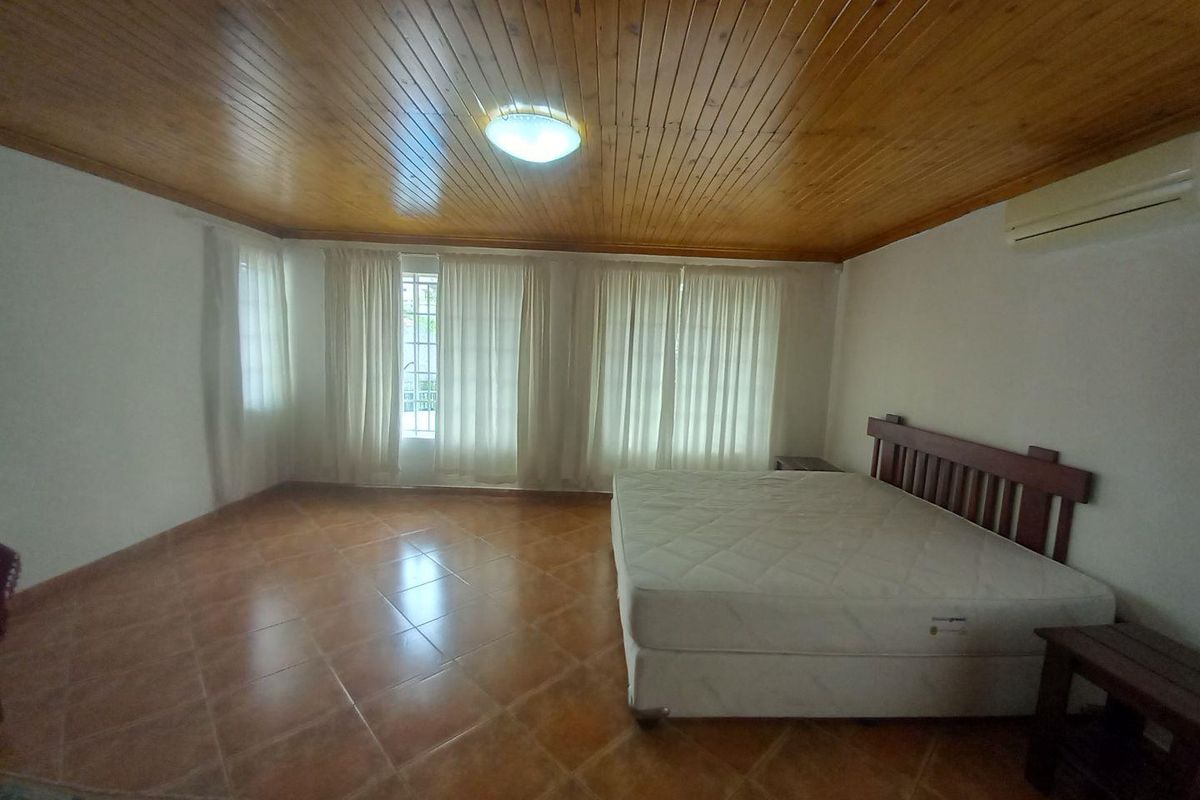 Spacious bedroom featuring a timber-clad ceiling, tiled flooring, and a wall-mounted air conditioning unit.
