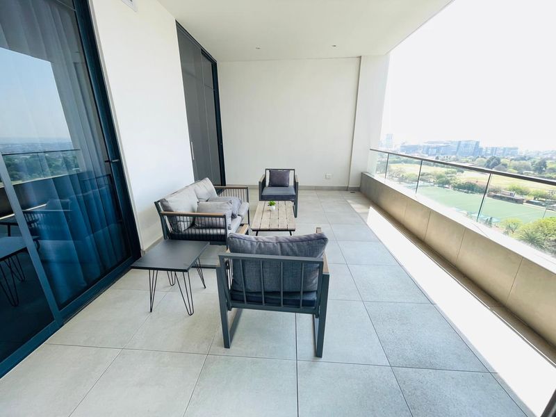 Spacious covered balcony featuring modern tiled flooring, a sleek glass balustrade, and large sliding doors providing seamless indoor-outdoor flow with expansive views.