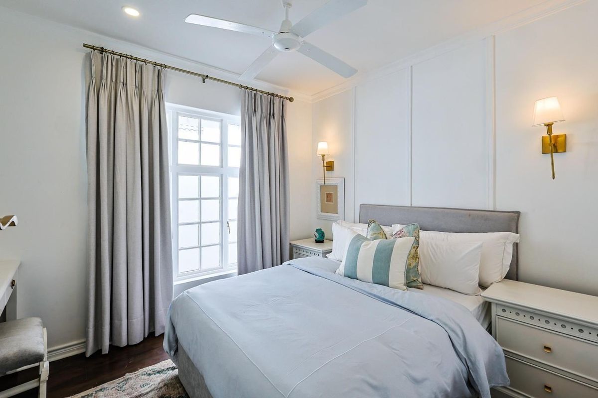 A well-appointed bedroom featuring classic wall paneling, a ceiling fan, and elegant wall-mounted lighting fixtures.