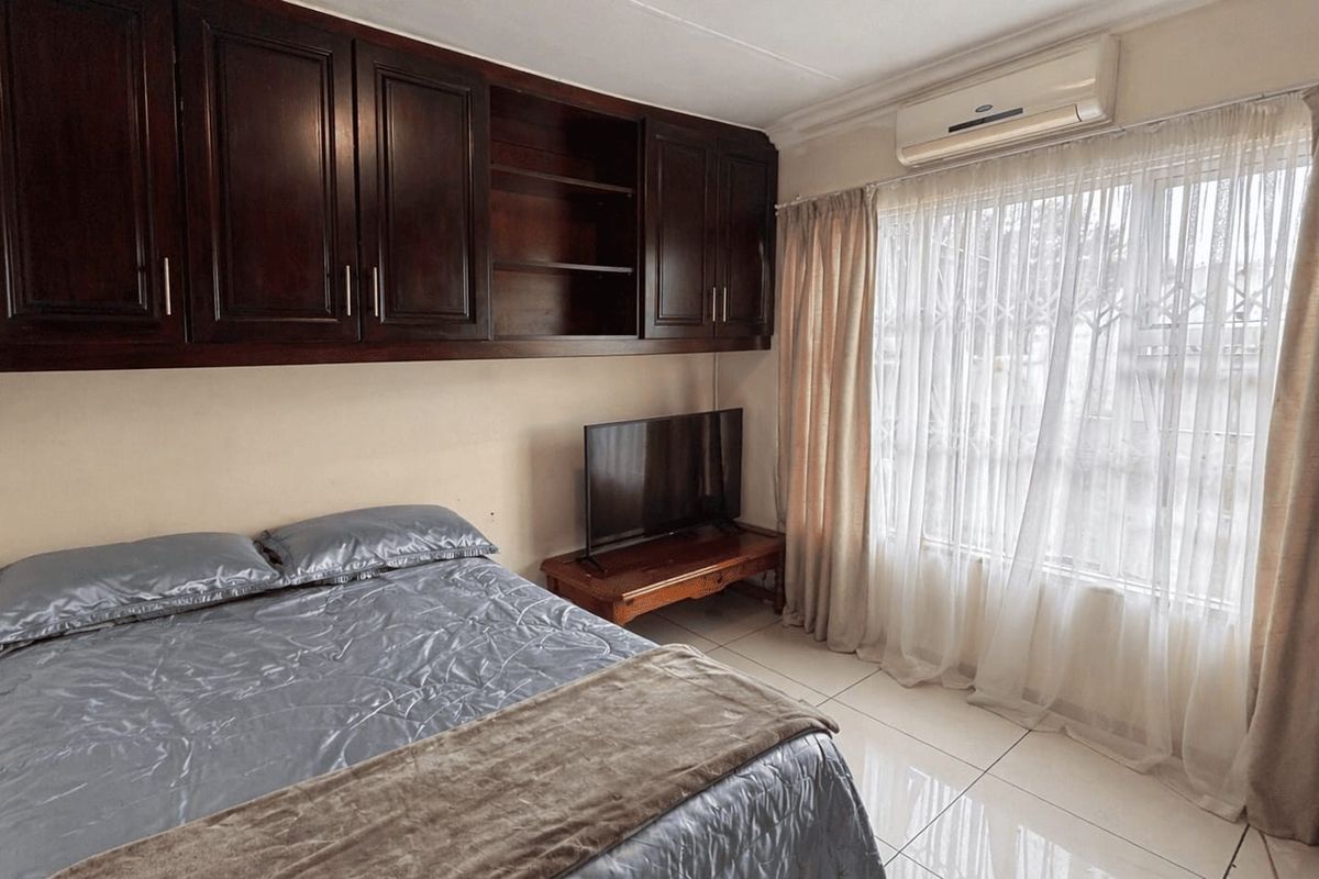 A bedroom featuring built-in dark wood cabinetry, tiled flooring, and a wall-mounted air conditioning unit.