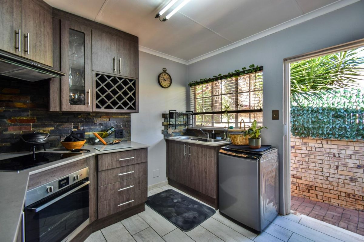 A functional kitchen featuring dark wood cabinetry, stone-tiled backsplash, built-in oven, hob, extractor fan, and direct access to an outdoor patio area.