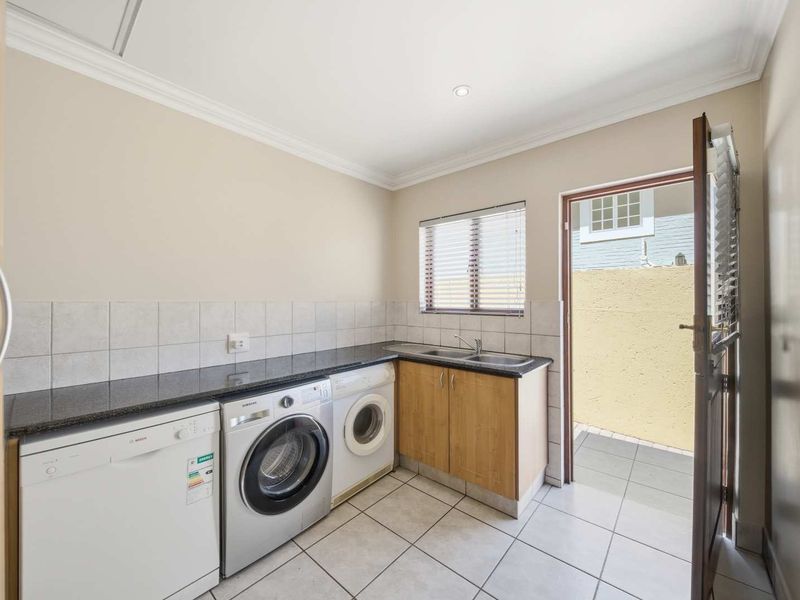 A functional laundry room featuring granite countertops, a double sink, tiled flooring, and direct access to an outdoor area.