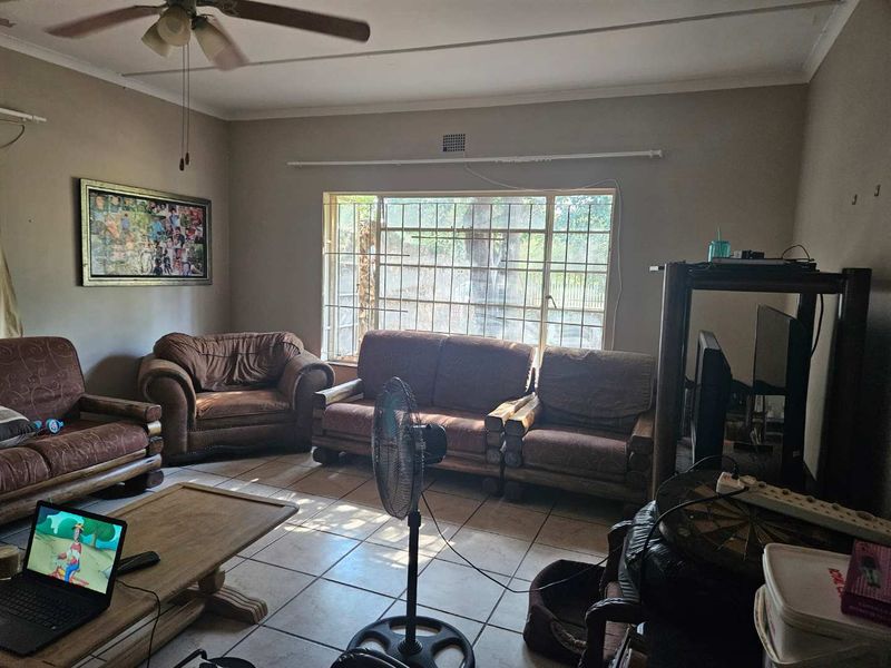 A living room featuring tiled flooring, a ceiling fan, and a large window with security bars, offering a functional space with potential for updates.