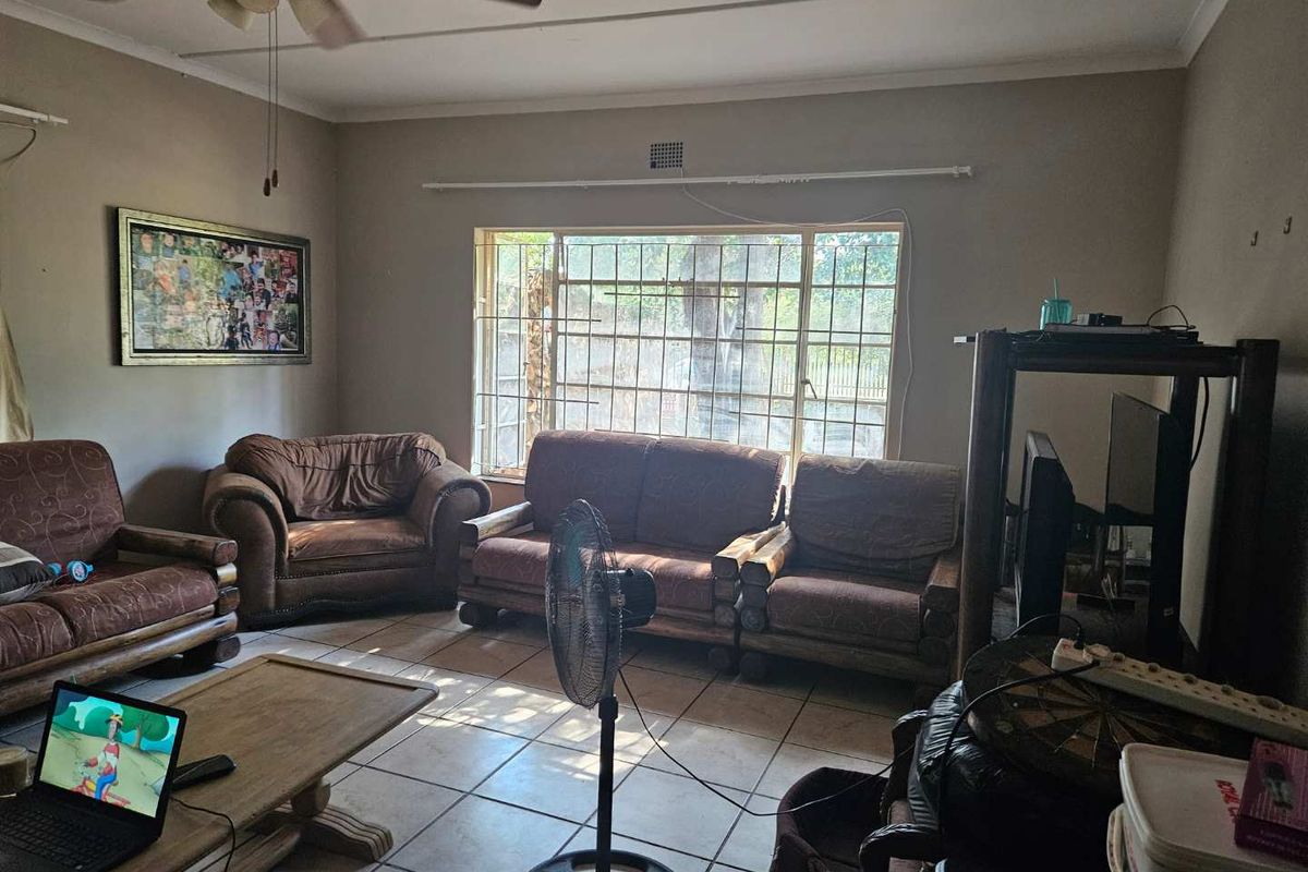 A living room featuring tiled flooring, a ceiling fan, and a large window with security bars, offering a functional space with potential for updates.