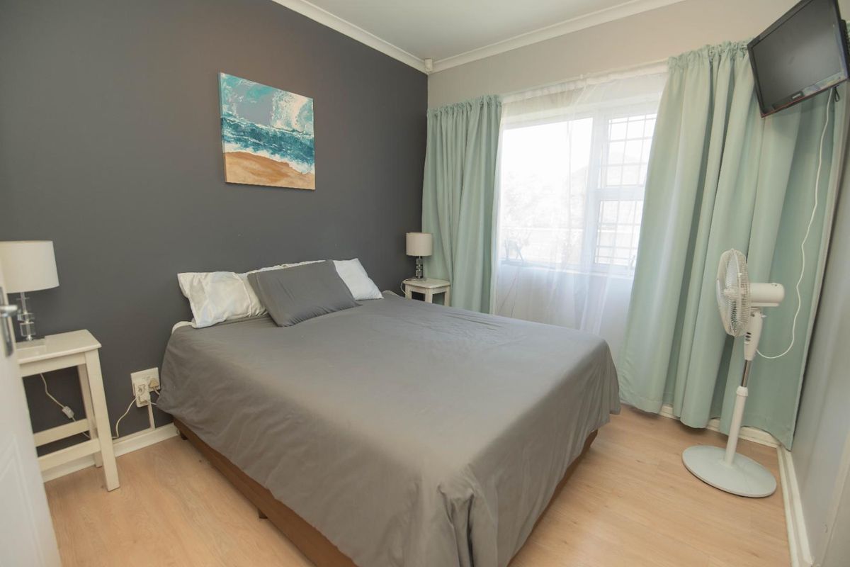 A cozy bedroom featuring light wood-look flooring, a dark accent wall, and a window with curtain treatments.