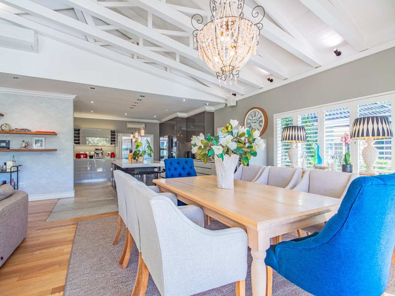 Spacious open-plan living and dining area featuring high vaulted ceilings with exposed beams, hardwood floors, and a modern kitchen with a central island.