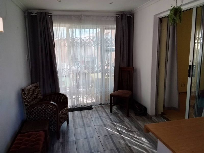 A living area featuring tiled flooring, recessed lighting, and a sliding glass door with a security gate leading to the exterior.