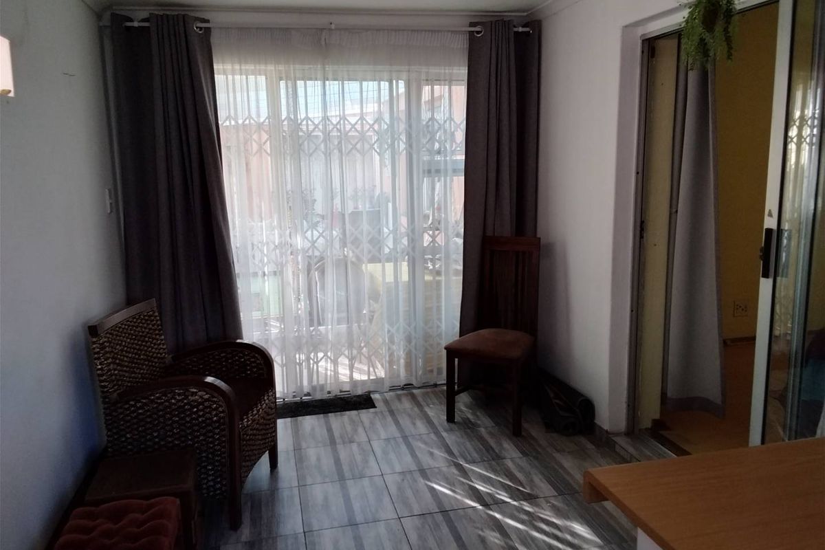 A living area featuring tiled flooring, recessed lighting, and a sliding glass door with a security gate leading to the exterior.