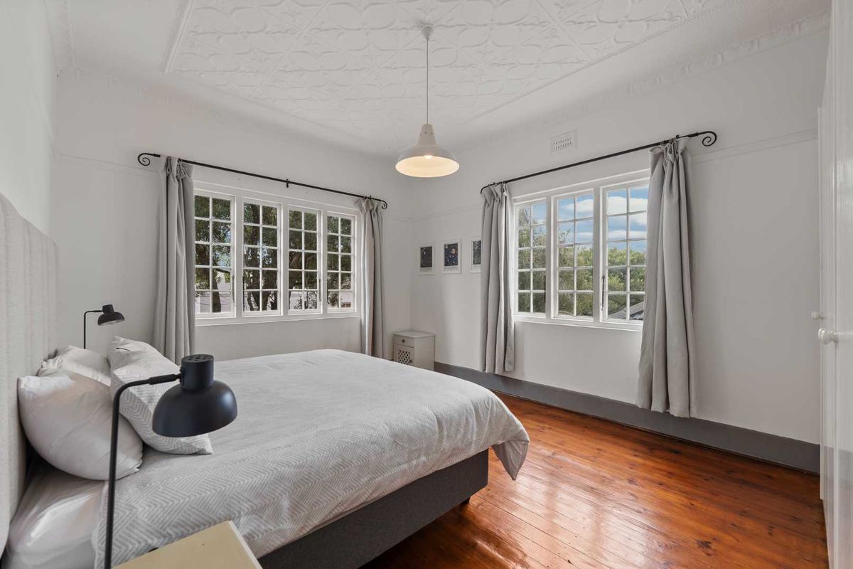A bright bedroom featuring polished timber flooring, a decorative pressed metal ceiling, and large multi-pane windows that provide ample natural light.