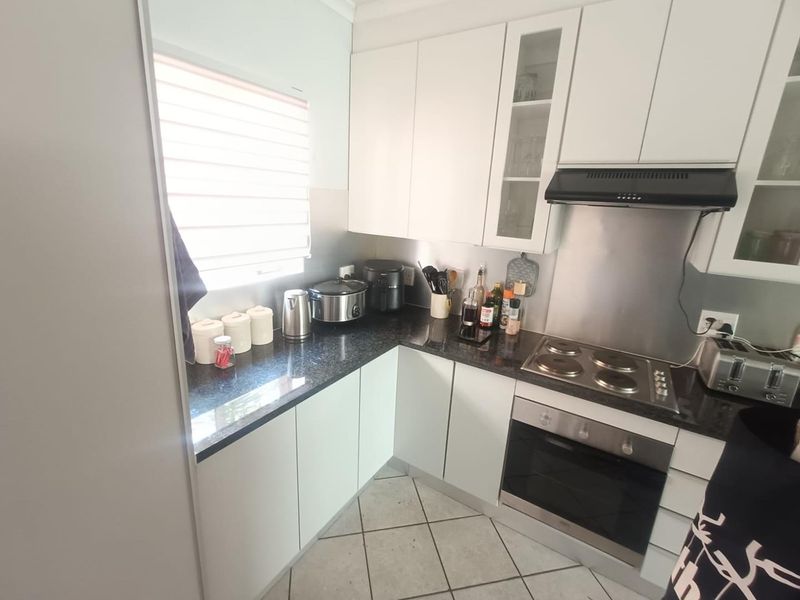 A functional kitchen featuring white cabinetry, granite countertops, a built-in oven, electric hob, and stainless steel splashback with tiled flooring.