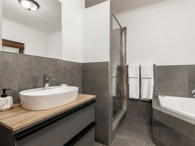 Modern bathroom featuring a vessel sink on a vanity cabinet, a glass-enclosed shower, and a built-in bathtub with contemporary grey tiling.