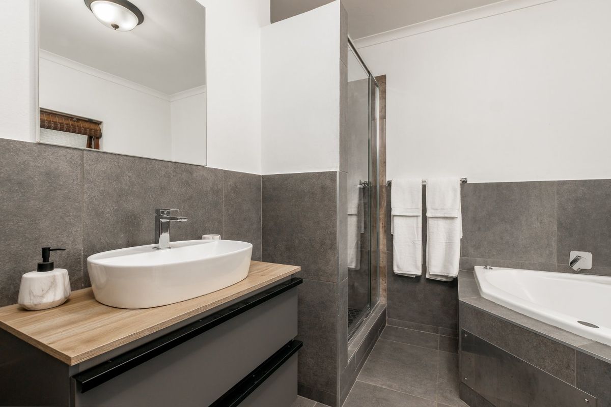 Modern bathroom featuring a vessel sink on a vanity cabinet, a glass-enclosed shower, and a built-in bathtub with contemporary grey tiling.