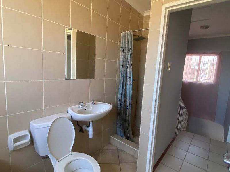 A functional bathroom featuring a wall-mounted basin, toilet, and a shower enclosure with tiled finishes throughout.