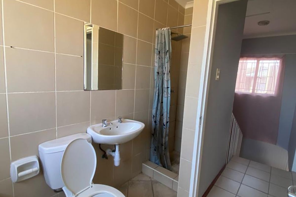 A functional bathroom featuring a wall-mounted basin, toilet, and a shower enclosure with tiled finishes throughout.