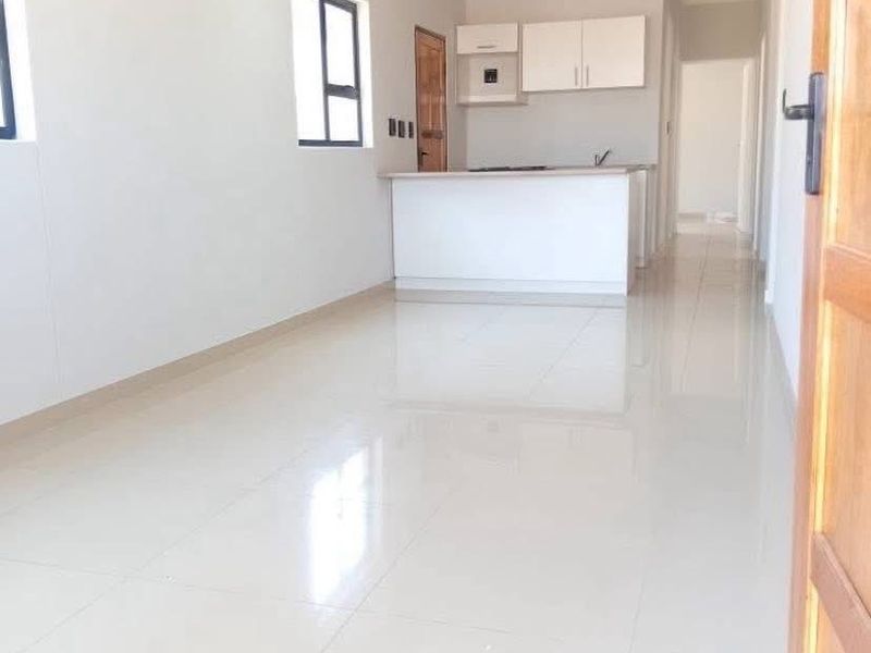 Bright and spacious open-plan living area featuring sleek tiled flooring, recessed lighting, and a functional kitchen with built-in cabinetry and a central island.