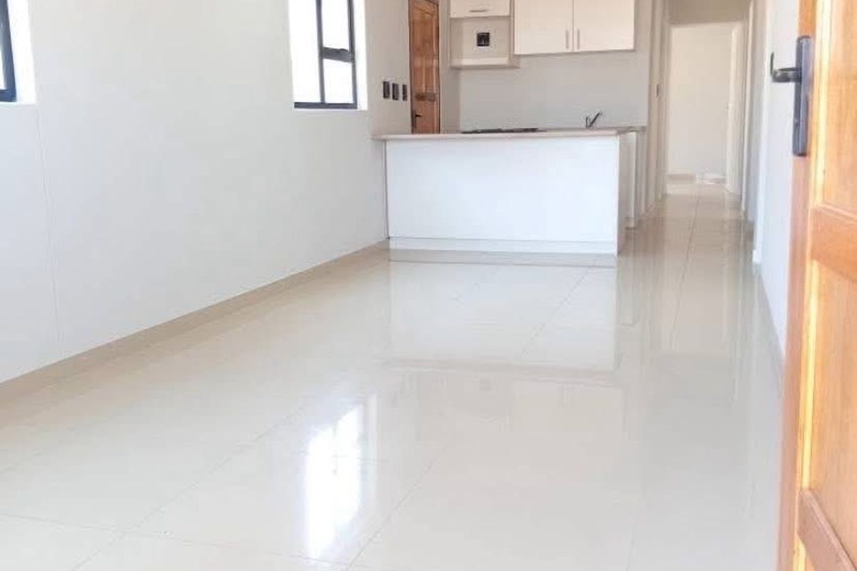 Bright and spacious open-plan living area featuring sleek tiled flooring, recessed lighting, and a functional kitchen with built-in cabinetry and a central island.