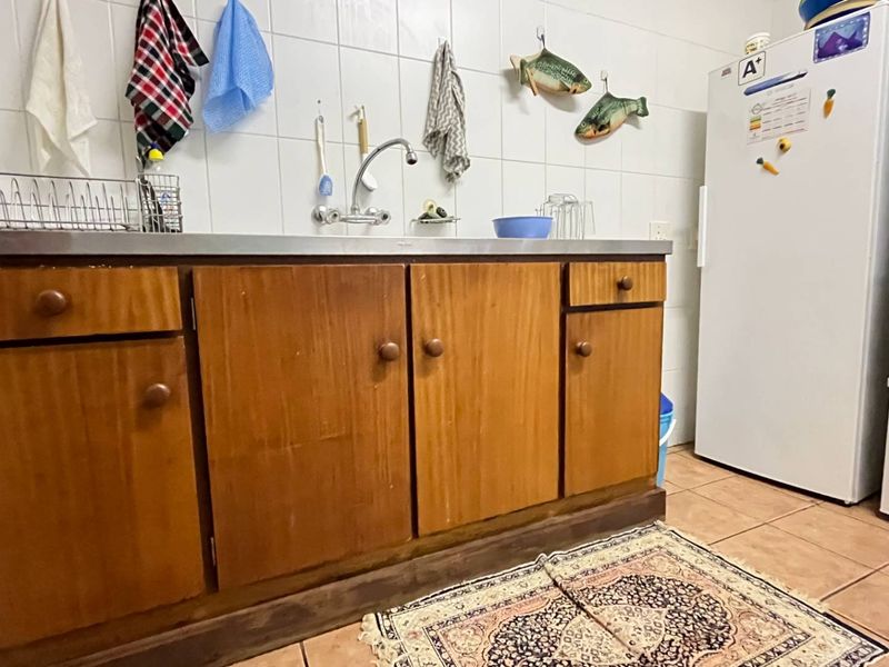A functional kitchen area featuring wooden cabinetry, a stainless steel sink with wall-mounted faucet, and tiled backsplash and flooring.