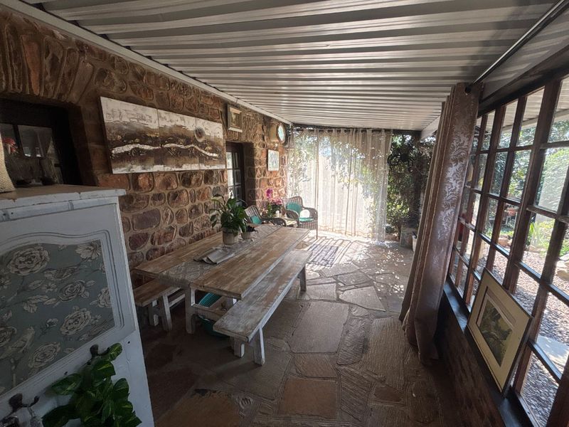 Covered patio area featuring rustic stone walls, flagstone flooring, and large timber-framed windows, providing a charming outdoor entertainment space.