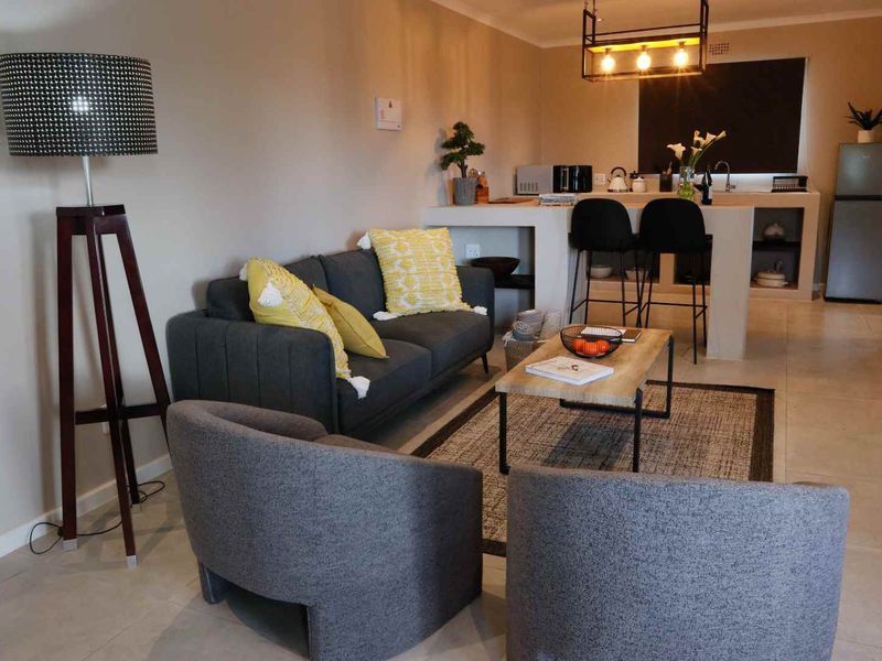 An open-plan living area featuring tiled flooring, a built-in breakfast bar, and modern pendant lighting, seamlessly connecting the lounge and kitchen space.