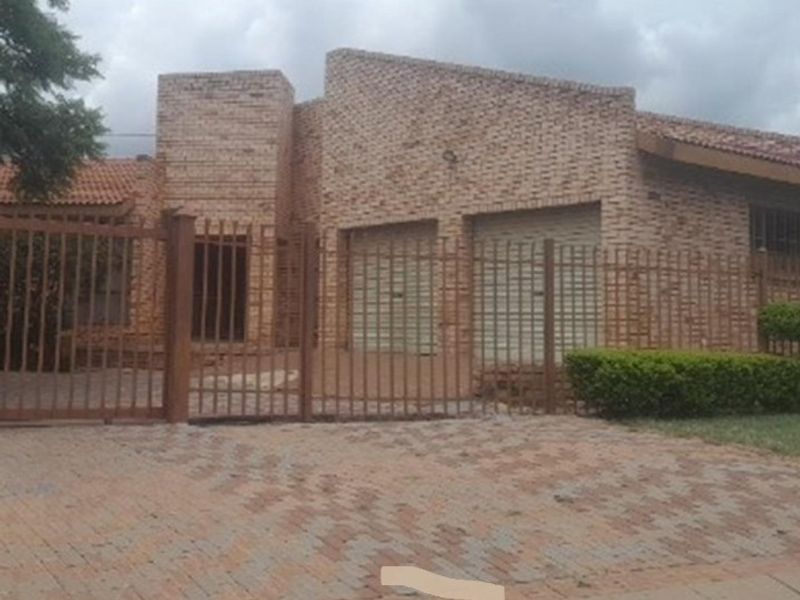 Front elevation of a face brick house featuring a double garage, paved driveway, and secure metal perimeter fencing.