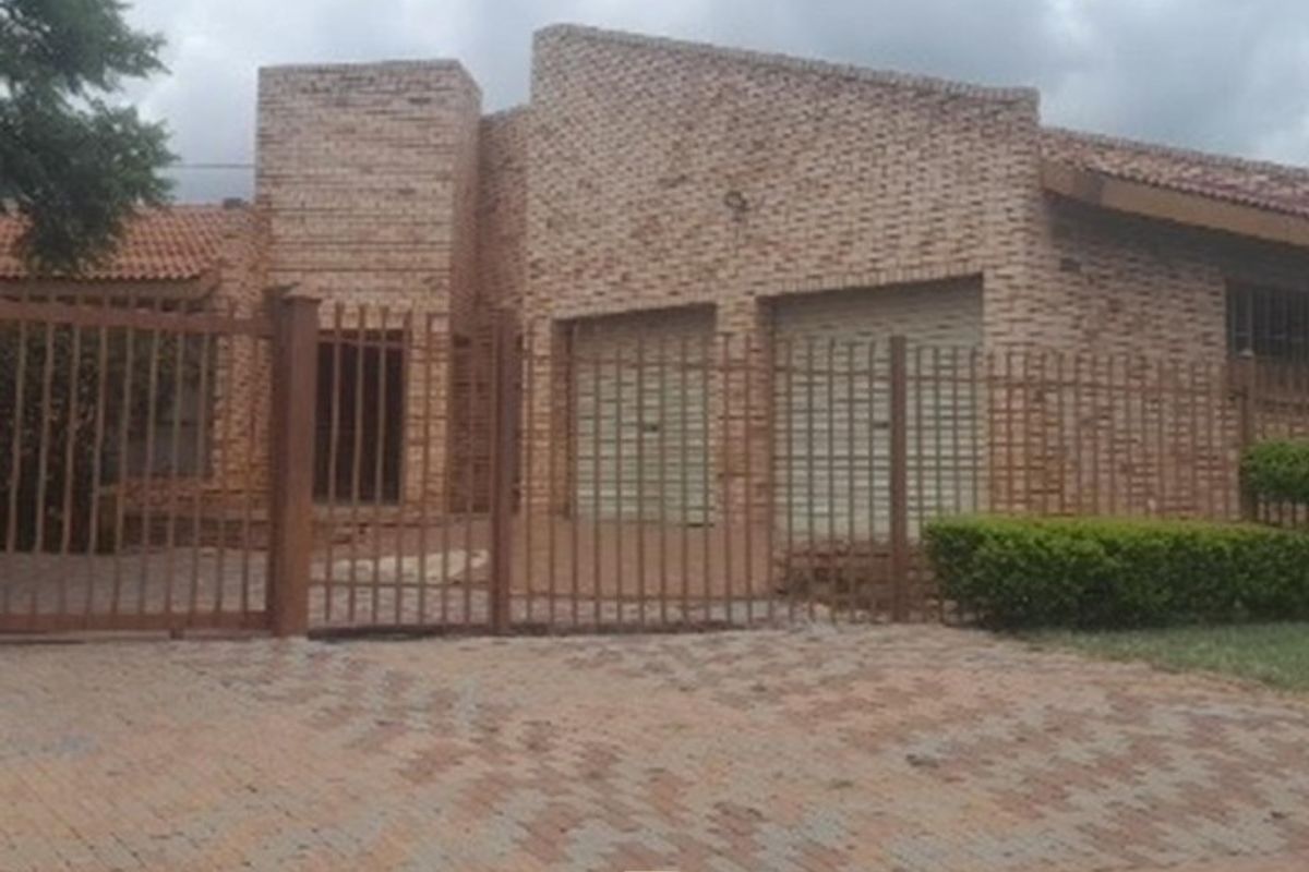 Front elevation of a face brick house featuring a double garage, paved driveway, and secure metal perimeter fencing.