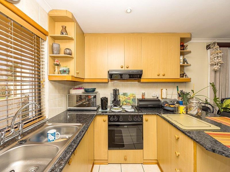 A functional kitchen featuring light wood-tone cabinetry, dark laminate countertops, a built-in oven, electric hob, and a double bowl stainless steel sink.