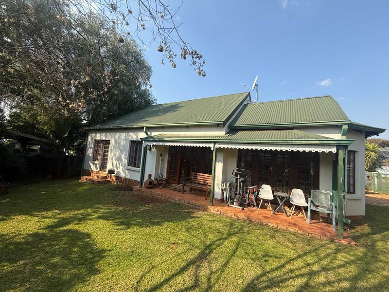 Rear view of the property featuring a covered patio with brick flooring, timber doors, and a well-maintained garden area.