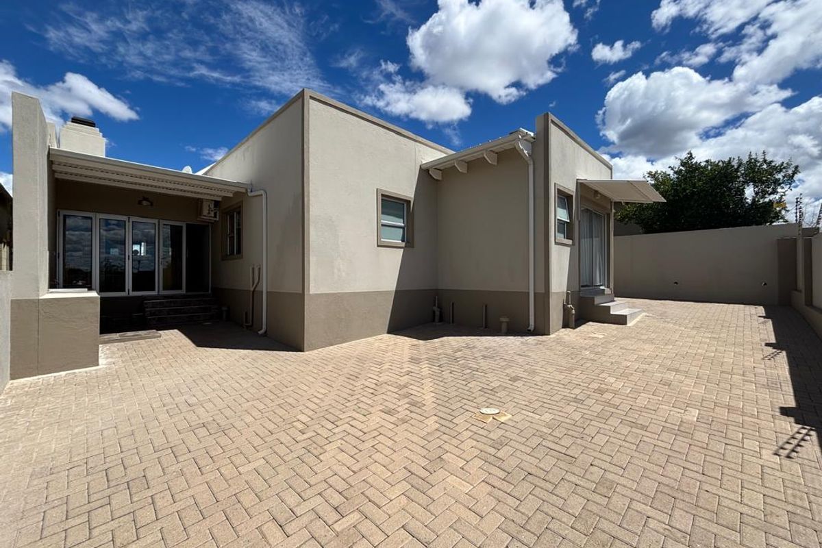 Rear view of the property featuring a paved courtyard, covered patio area, and exterior building facade with modern finishes.