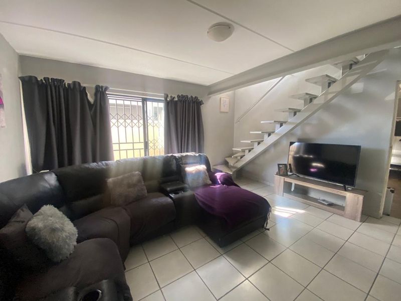 Open-plan living area featuring tiled flooring, a staircase, and a sliding glass door with security gate leading to the exterior.