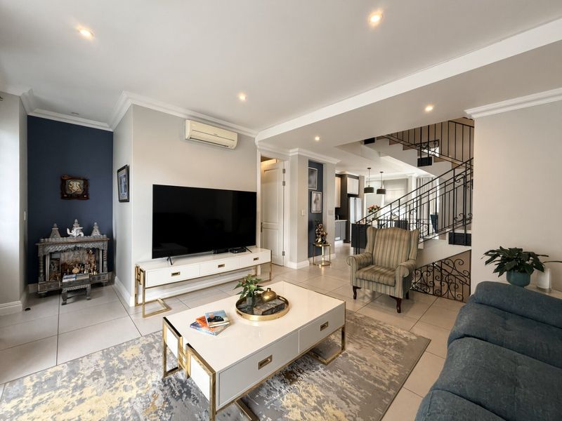 Spacious open-plan living area featuring tiled floors, recessed lighting, crown molding, and an elegant wrought iron staircase leading to the upper level.