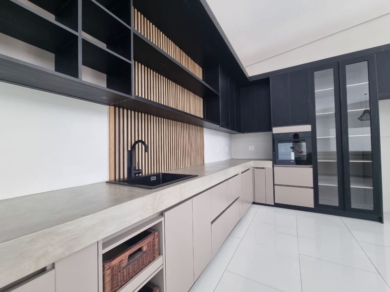 Modern kitchen featuring sleek two-tone cabinetry, concrete countertops, integrated oven, and stylish slatted wood wall detailing with ample storage space.