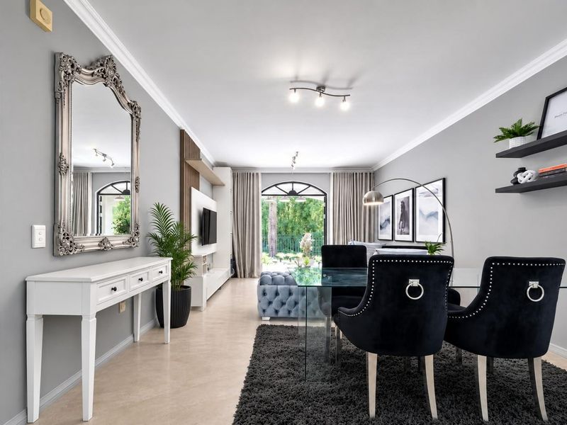 A bright and modern open-plan living and dining area featuring neutral walls, crown molding, tiled floors, and a large arched glass door to the exterior.