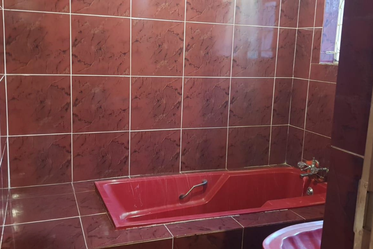 A bathroom featuring a built-in bathtub surrounded by dark red textured wall and floor tiles.