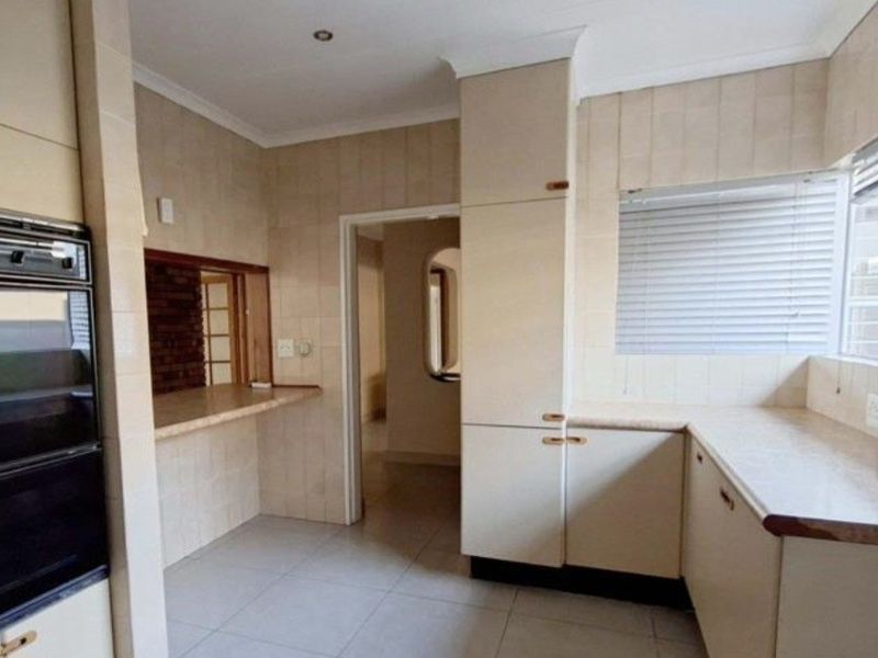 A functional kitchen featuring built-in cabinetry, tiled splashbacks, and a convenient pass-through window, offering a clean, neutral space ready for modernization.