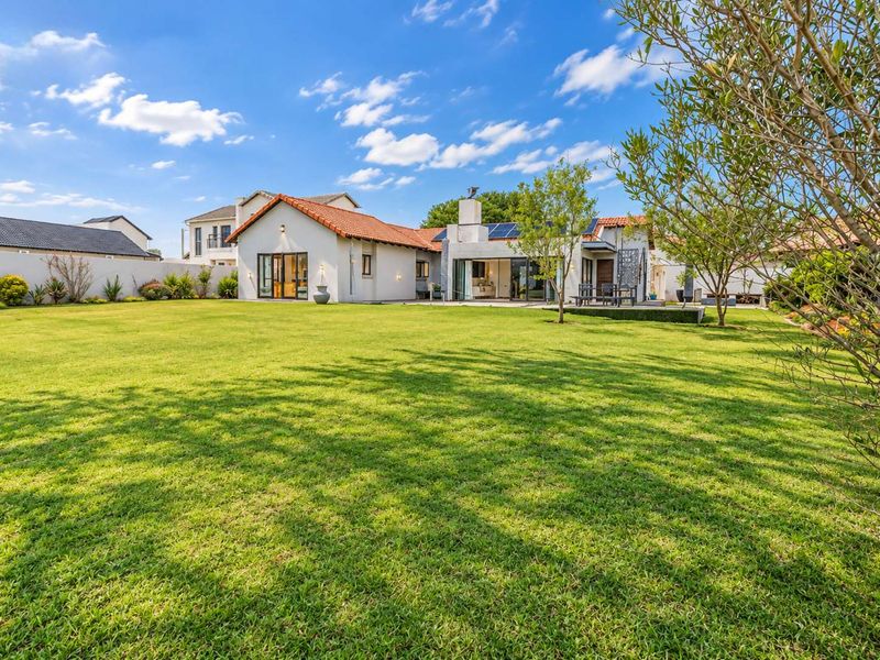 Spacious rear garden view featuring a well-maintained lawn, established landscaping, and the rear elevation of the house with terracotta roof tiles and solar panels.