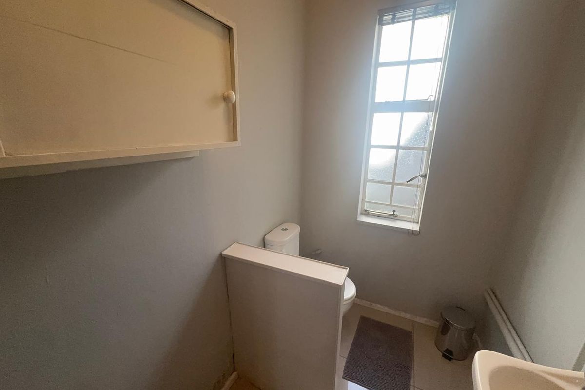 A compact guest bathroom featuring a toilet, wall-mounted storage cabinet, and a small window providing natural light.