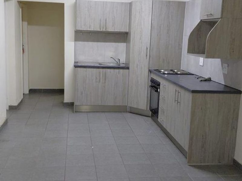 A clean, functional kitchen featuring light wood-grain cabinetry, dark laminate countertops, built-in oven, hob, and tiled flooring in an open-plan layout.