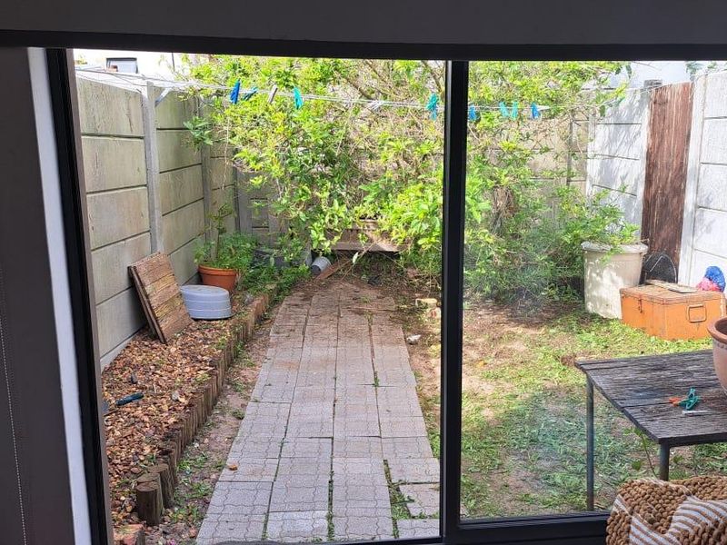 View from an interior sliding door looking out onto a rear garden area with a paved path and perimeter concrete walling.